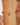 Gold bracelet with green and red beads on a wrist against a neutral background