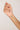 Hand holding a delicate gold necklace with small colored beads against a plain background