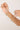 Hand holding a delicate gold necklace with green beads against a light background