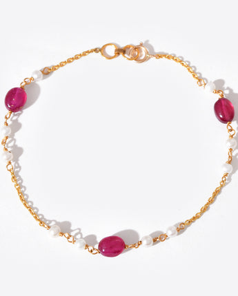 Bracelet with gold chain, white beads and pink stones on a white background