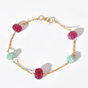 Bracelet with pink and green beads on a gold chain against a white background