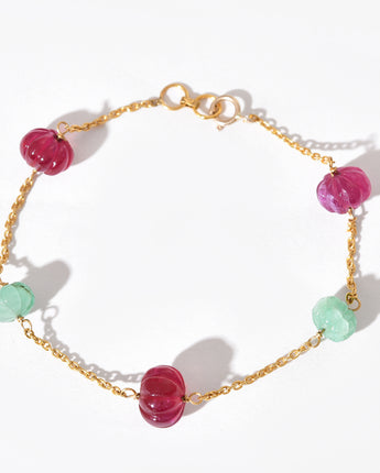 Bracelet with pink and green beads on a gold chain against a white background