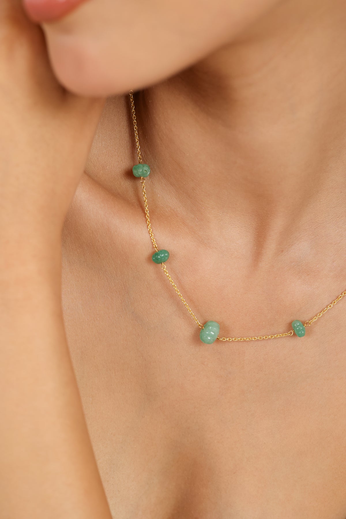 Gold necklace with green gemstones worn by a person