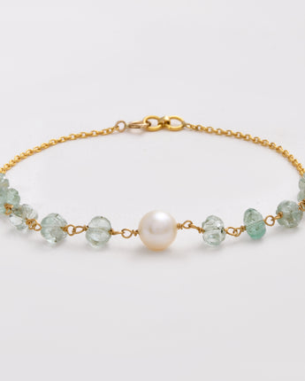 Gold bracelet with green beads and a pearl on a light gray background