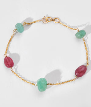 Bracelet with gold chain and green and pink beads on a white background