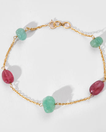 Bracelet with gold chain and green and pink beads on a white background